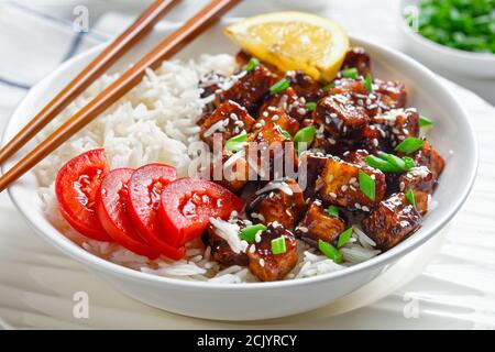 Teriyaki gebackenen Tofu mit Reis bestreut von Frühlingszwiebeln, Sesam, japanische Küche, serviert mit Reis, Tomate, Zitrone auf einer weißen Schüssel mit c Stockfoto