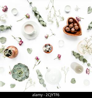 Arbeitsbereich mit Rosenknospen, Eukalyptus-Blätter, saftig, Tee, Tasse Kakao, Süßigkeiten auf weißem Hintergrund. Flach liegend, Ansicht von oben, Arbeitsplatz im Home Office Stockfoto