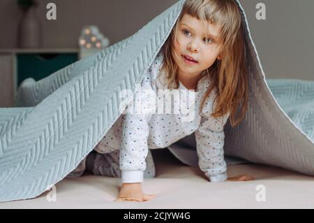 Happy schönes kleines Mädchen mit Spaß Zeit auf dem Bett unter der Decke im Schlafzimmer liegen. Stockfoto