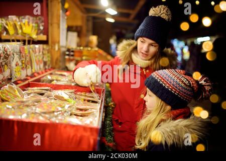 Nette junge Schwestern Spezialitäten Auswahl auf den traditionellen Weihnachtsmarkt in Riga, Lettland. Kinder kaufen Candy und Cookies auf Weihnachten. Happy Family Zeit an kühlen Stockfoto