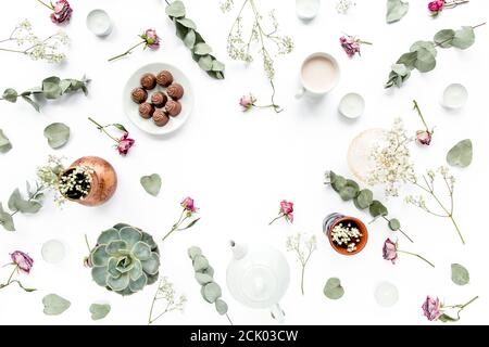 Arbeitsbereich mit Rosenknospen, Eukalyptus-Blätter, saftig, Tee, Tasse Kakao, Süßigkeiten auf weißem Hintergrund. Flach liegend, Ansicht von oben, Arbeitsplatz im Home Office Stockfoto