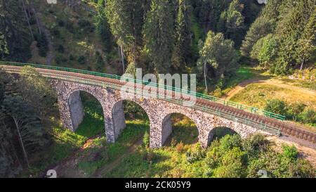 Luftaufnahme von oben auf Stein Eisenbahnviadukt in einem kleinen Dorf von Pernink, Tschechische republik. Alte tschechische Eisenbahnlinie. Alte Bogenbrücke Stockfoto