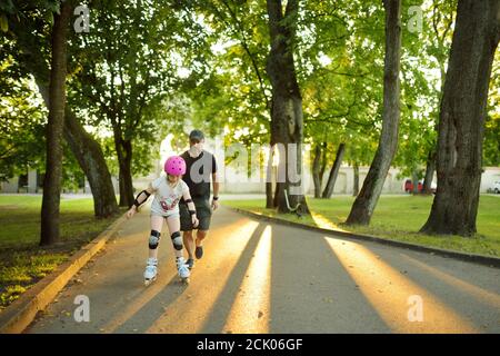 Vater lehrt seine junge Tochter Rollschuh an schönen Sommertag in einem Park. Kind trägt Schutzhelm genießen Rollschuhfahren im Freien Stockfoto