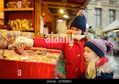 Nette junge Schwestern Spezialitäten Auswahl auf den traditionellen Weihnachtsmarkt in Riga, Lettland. Kinder kaufen Candy und Cookies auf Weihnachten. Happy Family Zeit an kühlen Stockfoto