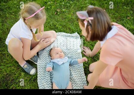 Zwei große Schwestern bewundern ihren liebenswerten kleinen Bruder. Zwei junge Mädchen mit ihrem neuen Baby Jungen Geschwister. Kinder mit großer Alterslücke. Großer Altersunterschied Stockfoto