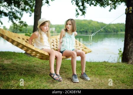 Nette junge Schwestern, die Spaß in der Hängematte am schönen Sommertag haben. Kinder entspannen im Sommerpark. Familienurlaub im Sommer. Stockfoto