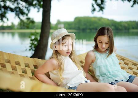 Nette junge Schwestern, die Spaß in der Hängematte am schönen Sommertag haben. Kinder entspannen im Sommerpark. Familienurlaub im Sommer. Stockfoto