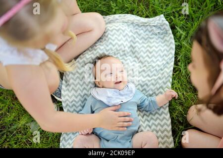 Zwei große Schwestern bewundern ihren liebenswerten kleinen Bruder. Zwei junge Mädchen mit ihrem neuen Baby Jungen Geschwister. Kinder mit großer Alterslücke. Großer Altersunterschied Stockfoto