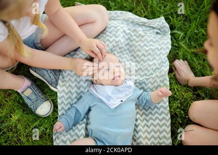 Zwei große Schwestern bewundern ihren liebenswerten kleinen Bruder. Zwei junge Mädchen mit ihrem neuen Baby Jungen Geschwister. Kinder mit großer Alterslücke. Großer Altersunterschied Stockfoto