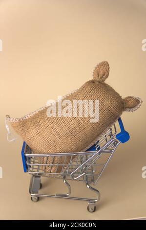 Ein Miniatur-Einkaufswagen enthält einen vollgefüllten Sackleinen, alles auf einem neutralen beigen Hintergrund Stockfoto