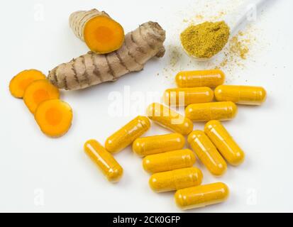 Kurkuma-Wurzel mit gelben Kapseln und einem Löffel Curcuma Pulver Auf einem weißen Teller Stockfoto