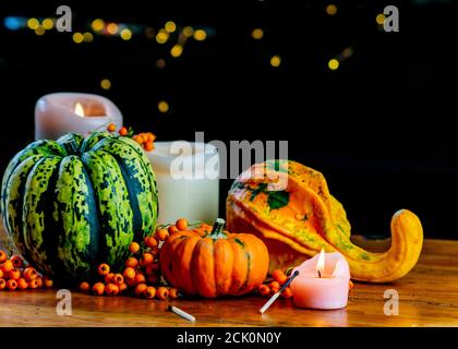 Vielfalt an Kürbissen, Vogelbeeren und Kerzen auf rustikalem Holztisch und schwarzem Hintergrund mit Bokeh. Herbst symbolische Gemüse in grün, gelb und Stockfoto