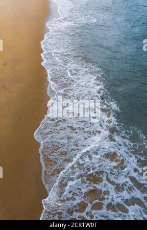 Von einem Pier aus hat man einen Blick auf die Wellen, die auf den Sandstrand schwassen. Stockfoto