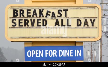 Ein Schild mit abgleitendem Buchstaben besagt, dass das Frühstück den ganzen Tag serviert wird, und ein anderes, das sagt, dass man vor einem Familienrestaurant zum Abendessen geöffnet hat Stockfoto