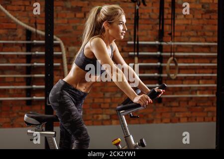 Pleasantblonde Frau ist mit exercycle in der Turnhalle.effektive Herz-Kreislauf-Übung. Stockfoto