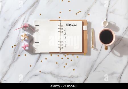 Notizbuch mit Wunschliste, Stift, Kaffeetasse, Geschenkschachteln, Gold funkelt auf weißem Schreibtisch Stockfoto