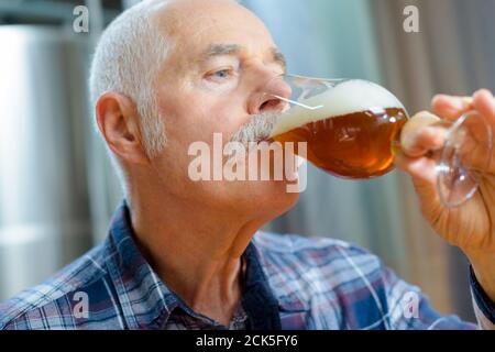 Senior-Brauer, der Bier im Glas verkostet Stockfoto