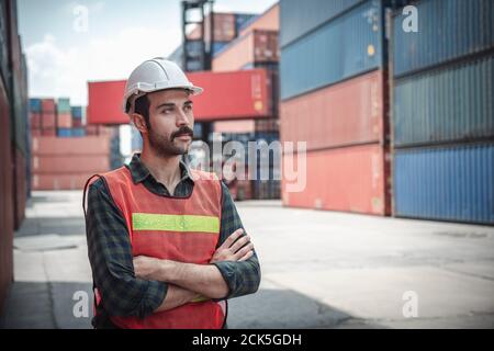 Portrait of Confident Transport Engineer man in Safety Equipment Standing in Container Ship Yard. Transport Engineering Management und Container Stockfoto