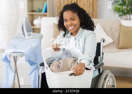 Frau im Mädchen im Rollstuhl mit Korb in der Nähe der Waschmaschine Stockfoto