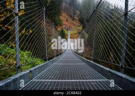 Hängebrücke aus Metall über dem schönen Rabby-Tal im Nebel irgendwo in Norditalien im Frühherbst. Stockfoto