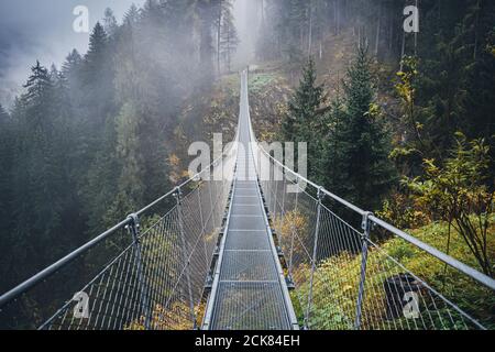 Hängebrücke aus Metall über dem schönen Rabby-Tal im Nebel irgendwo in Norditalien im Frühherbst. Stockfoto