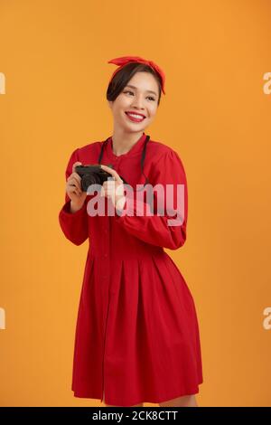 Schöne fröhlich junge asiatische Frau halten Retro-Stil Kamera und die Fokussierung auf Sie mit Lächeln, während vor orangenen Hintergrund Stockfoto