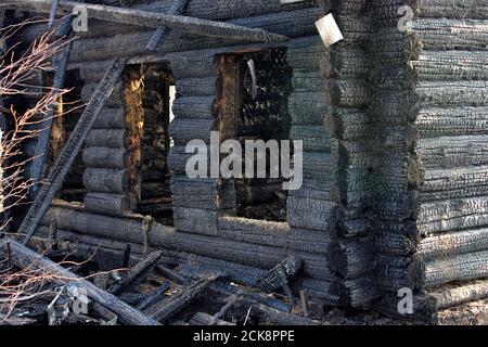 Nach dem Feuer - verbranntes Haus. Schwarz verbrannte Holzwände, viele beschädigte Bretter und Müll. Sonniger Sommertag. Stockfoto