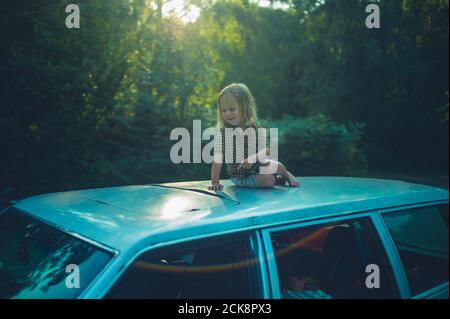 Ein kleiner Vorschulkinder sitzt auf dem Dach eines Auto bei Sonnenuntergang Stockfoto