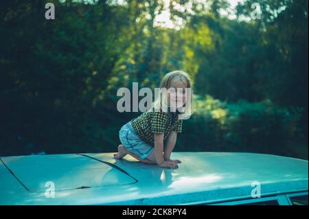 Ein kleiner Vorschulkinder sitzt auf dem Dach eines Auto bei Sonnenuntergang Stockfoto