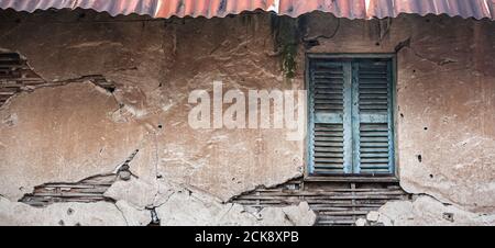 Verlassene Betonwand Textur des alten Hauses, alten Bambus in einem alten Beton mit rissig und erodiert, alte blaue Holzfenster, rostig verzinkt. Stockfoto