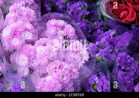 Frische blühende Blumen in einem lokalen Blumengeschäft in einem täglichen Markt, schöne rosa Nelken, rote Rosen und lila Statice Bündel. Draufsicht. Stockfoto