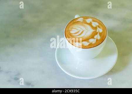 Nahaufnahme einer Tasse Latte befindet sich auf dem Marmortisch, eine weiße Keramik Tasse Kaffee Latte mit Latte Art. Flache Lay. Draufsicht. Stockfoto