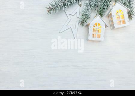 weihnachtsbaum Zweig mit Feiertagsbeleuchtung in Form von Häusern und Holzstern geschmückt. Weiß Neujahr Hintergrund Stockfoto