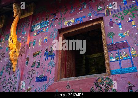 Antiker Tempel des Wat Xieng Thong in der Dämmerung leuchtet warmes Licht auf Buntglas an der Wand und Holzfenster. Weltkulturerbe, Luang Prabang, Laos. Stockfoto