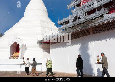 Asiatische buddhistische Pilger, die mit Blumenstrauß um die alte Pagode des Wat Phrathat Doi Kong Mu, Mae Hong Son, Thailand, wandern. Stockfoto