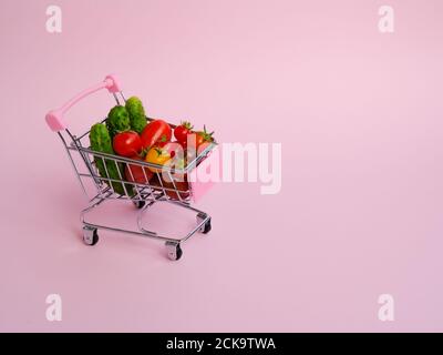 Rosa Lebensmittelkarren voller Tomaten und Gurken auf rosa Hintergrund Stockfoto