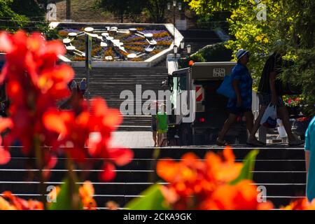 Sewastopol Stadtzentrum mit Menschen und Autos am 13. August 2020. Reinigung der Straße mit einem kleinen Hummel Auto. Bunte Stadtlandschaft. Rote Kannas in A Stockfoto