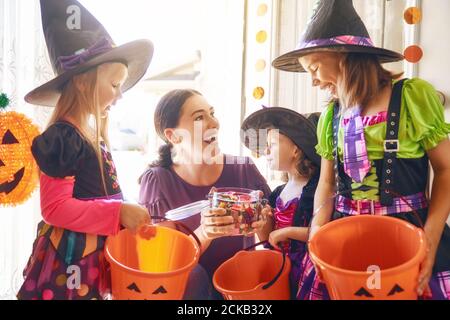 Glückliche Familie feiert Halloween! Junge Mutter behandelt Kinder mit Süßigkeiten. Lustige Kinder in Faschingskostümen. Stockfoto