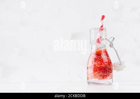 Frische Erdbeerlimonade mit geschnittener Beere, Sodawasser, Stroh in transparenter Yoke-Flasche auf weichem hellweißem Holztisch, Kopierraum. Stockfoto