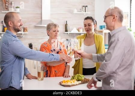 Familie klirrende Weingläser in der Küche während des Mittagessens. Feiern Toasting zusammen glückliche Großfamilie Stockfoto