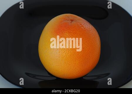 Früchte sind Zitrusfrüchte. Orange graue Frucht auf einem schwarzen Teller. Stockfoto
