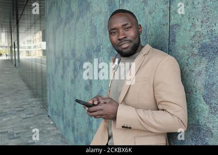 Porträt eines afrikanischen Mannes in Anzug lächelnd an der Kamera während Mit seinem Mobiltelefon im Freien Stockfoto