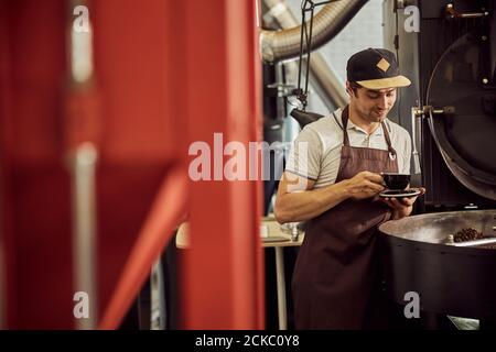 Hübscher männlicher Arbeiter in der Schürze, der Kaffee trinkt Stockfoto