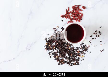 Roter Hibiscus-Tee in Glas-Tasse und Goji-Beeren Draufsicht auf weißem Marmor Hintergrund. Gesunde Ernährung, Entgiftung. Stockfoto