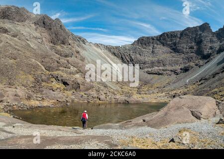 Einreisende weibliche Wandererin durch die Gewässer von Coire Lagan mit Cuillin Ridge oben in den Black Cuillin Mountains, Isle of Skye, Schottland, Großbritannien Stockfoto