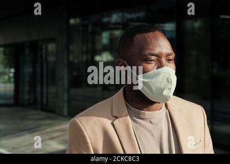 Afrikanischer junger Geschäftsmann in Schutzmaske im Freien in der Nähe der Bürogebäude Stockfoto