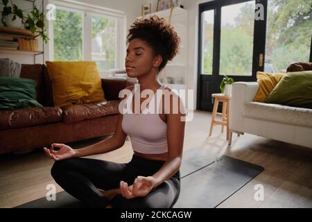 Junge schwarze Frau beim Yoga zu Hause im Lotussitz Stockfoto
