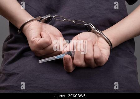 Drogenhandel, ein Mann in Handschellen mit einer Spritze. Stockfoto