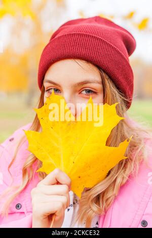 Glückliche junge Frau spielt mit fallenden gelben Blättern in schönen Herbstpark auf Naturwanderungen im Freien. Teenager-Mädchen hält Herbst orange Ahornblatt Stockfoto