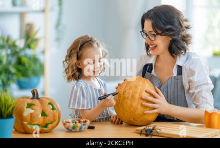 Glückliche Familie bereitet sich auf Halloween vor. Mutter und Kind schnitzen Kürbisse zu Hause. Stockfoto